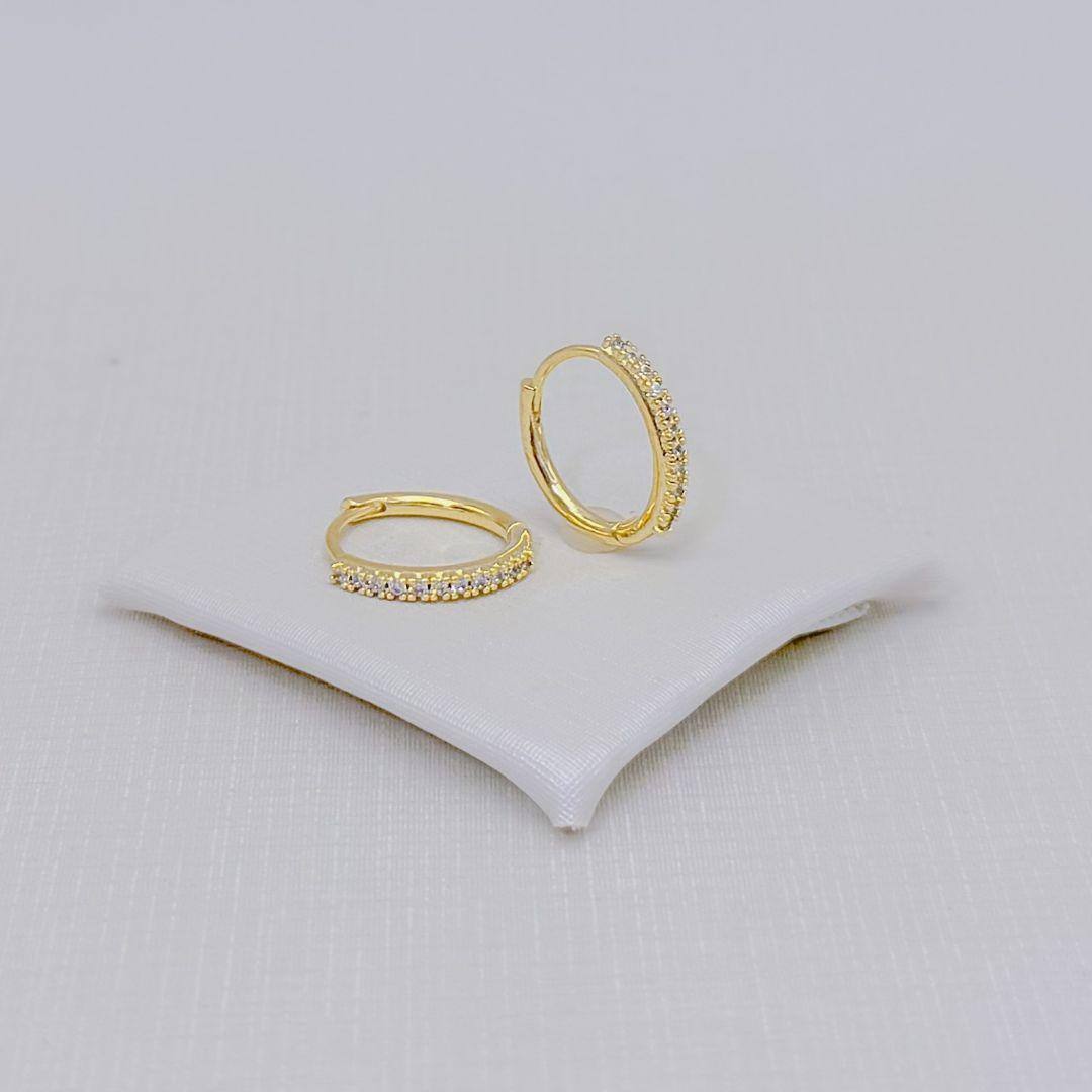 05.3344.1.O - (Tam. G) Argola de fio redondo em formato U com parte frontal cravejada em garras altas. Argola banhada a ouro.